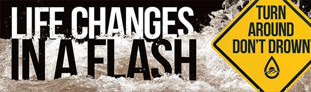 Banner with the text 'LIFE CHANGES IN A FLASH' alongside a yellow warning sign that reads 'TURN AROUND DON’T DROWN' over a background of flowing floodwaters.