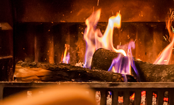 Close-up of a wood-burning fireplace with flames dancing on the logs, casting a warm glow in a dark setting.