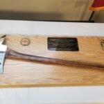 A ceremonial axe on a wooden plaque with a firefighter emblem and small firefighter figure. A metal plate reads: Presented to Chief Tommy Erickson for Your Leadership and Dedicated Service During the Brianhead Fire of Summer.