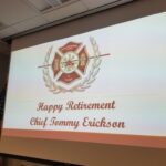 A presentation slide reads, Happy Retirement Chief Tommy Erickson, featuring a firefighter emblem with the text 8 Years. An American flag is partially visible on the left.