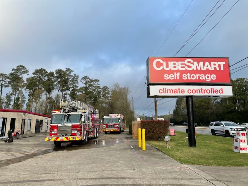 Fire trucks are parked outside a CubeSmart self-storage facility with a prominent sign that reads climate controlled. The background features trees and a cloudy sky.