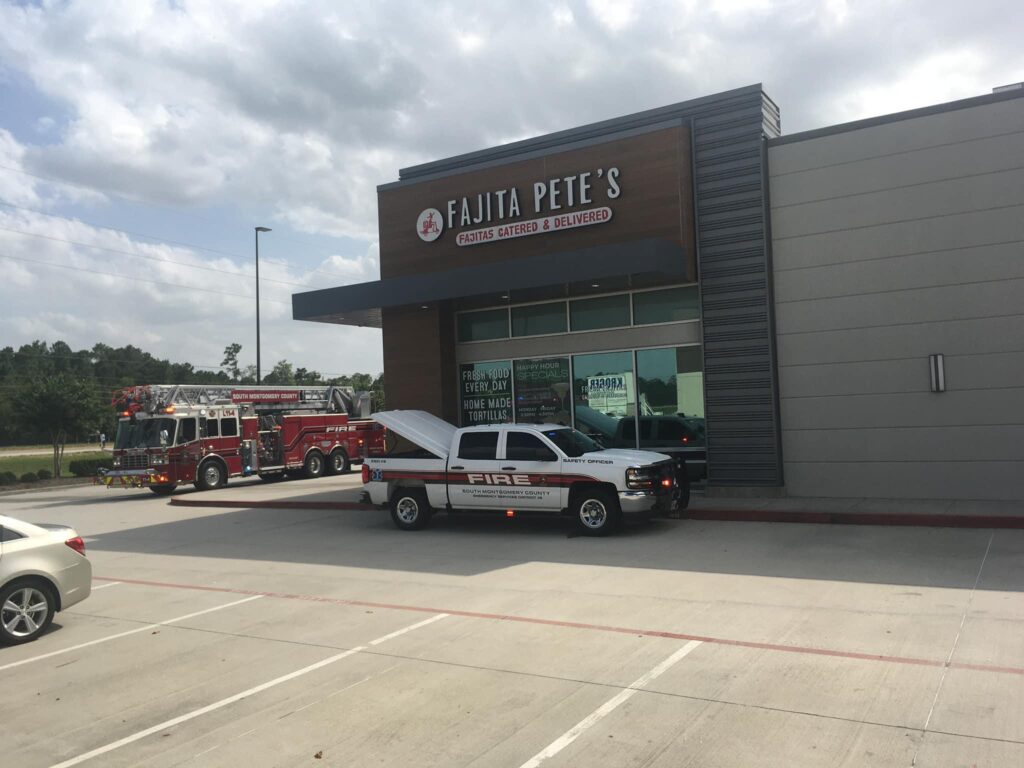 A fire department truck and SUV are parked outside a restaurant named Fajita Petes. The sky is cloudy, and the restaurant is in a single-story building with large windows. Several other cars are parked nearby.