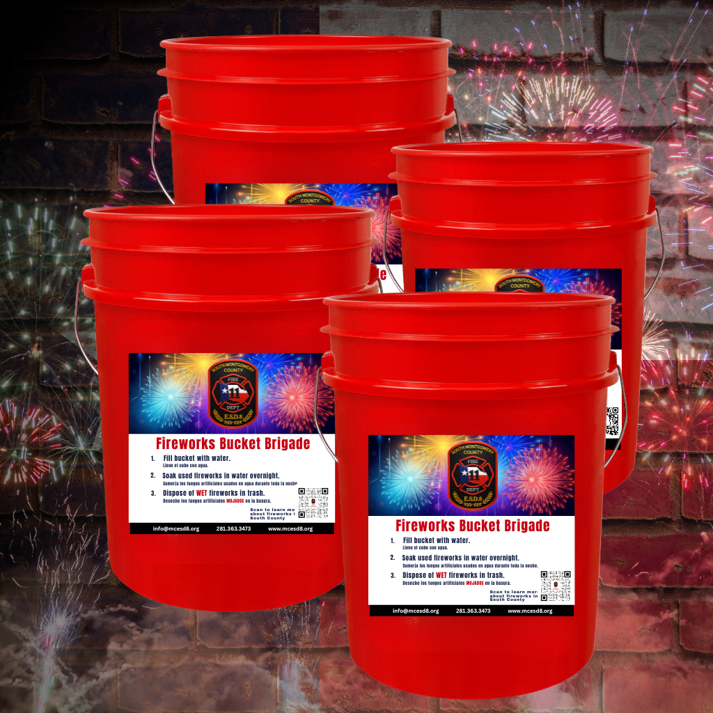 Four red buckets with Fireworks Bucket Brigade labels are arranged in front of a brick wall with colorful fireworks in the background. The buckets include firework safety instructions.